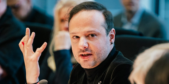 Francesco Cavallo sitzt auf der Konferenz am Tisch und gestikuliert mit der rechten Hand.