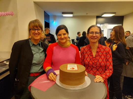 Julia Teschade, Mona Motakef and Christine Wimbauer behind a bar table with a cake decorated with the book cover on it.