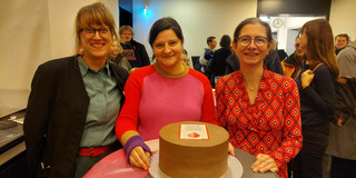 Julia Teschade, Mona Motakef and Christine Wimbauer behind a bar table with a cake decorated with the book cover on it.
