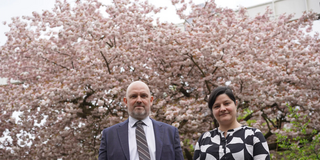 Christian Deindl und Mona Motakef are standing in front of a blooming tree with pink flowers.